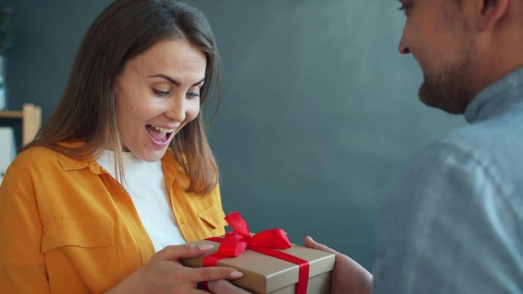 A woman smiling as she receives a gift box with a red ribbon.