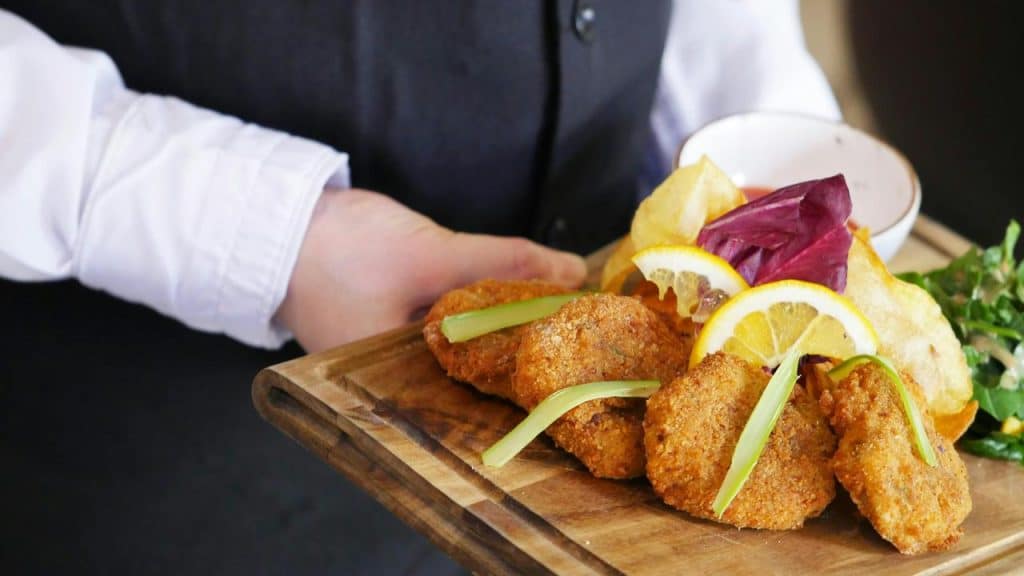 A server holding a wooden board with fried food, lemon slices, and salad.
