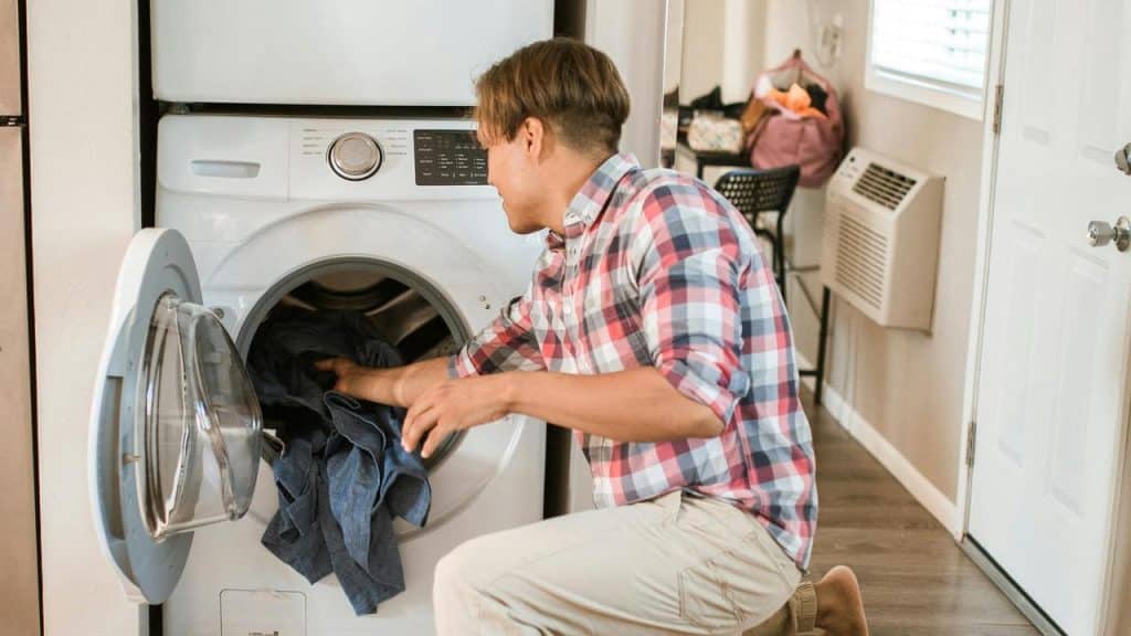 A man loading clothes into a washing machine at home.