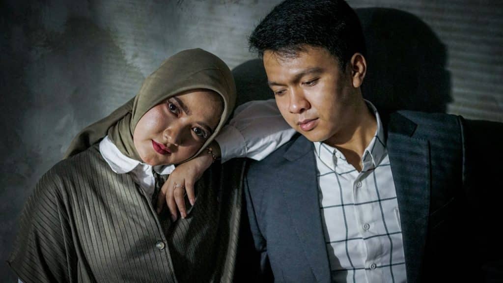 A woman putting her arm on a man’s shoulder while they are standing close to each other.
