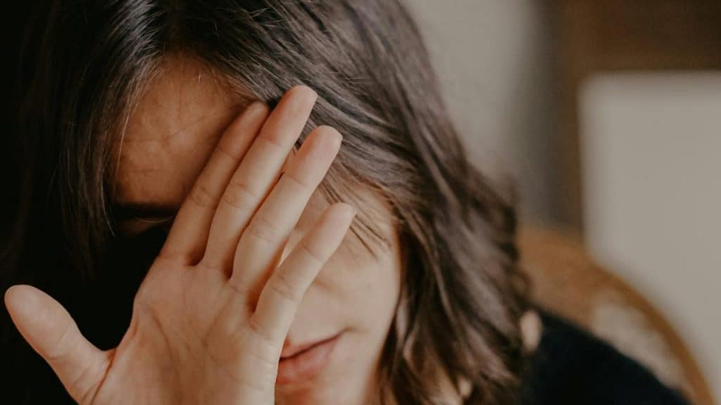 A person covering part of their face with one hand indoors.