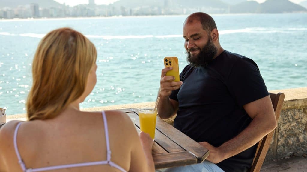 A man taking photo of his girlfriend while they are on a date near a lake.