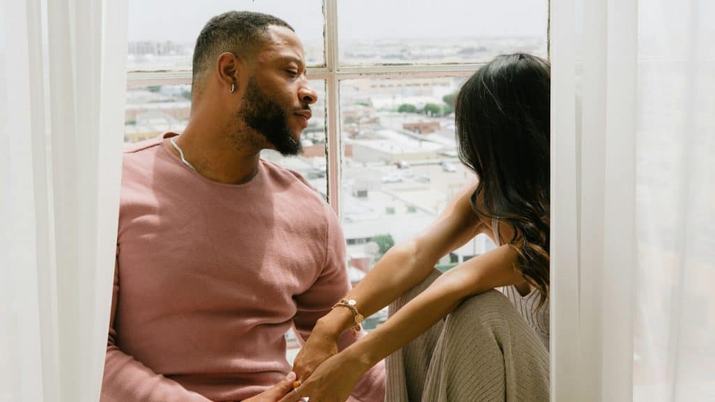 A couple sitting near a window in their room.