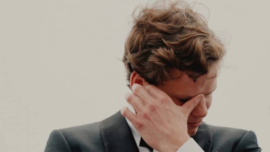 A man in a tuxedo holds his hand to his face.