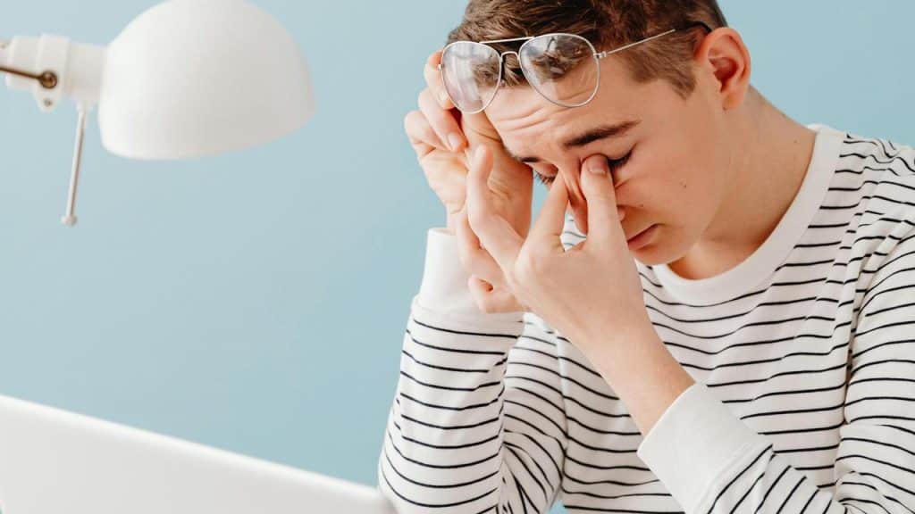 A man pinching his face with stress while holding his eyeglasses.