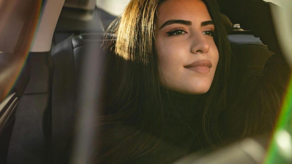 A woman gazing out a car window in warm sunlight.