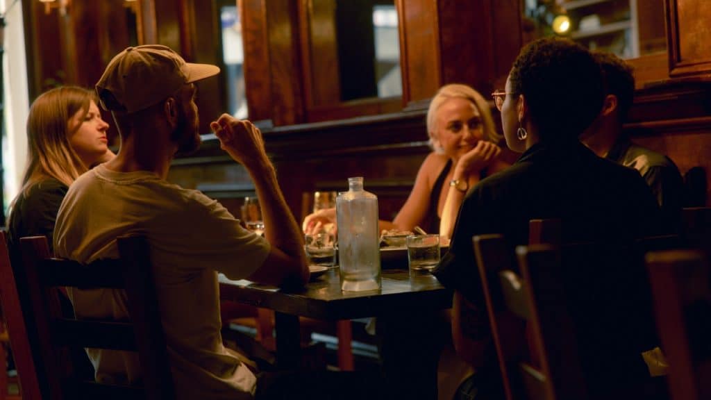 A group of people sits around a dark wooden table in a dimly lit restaurant.