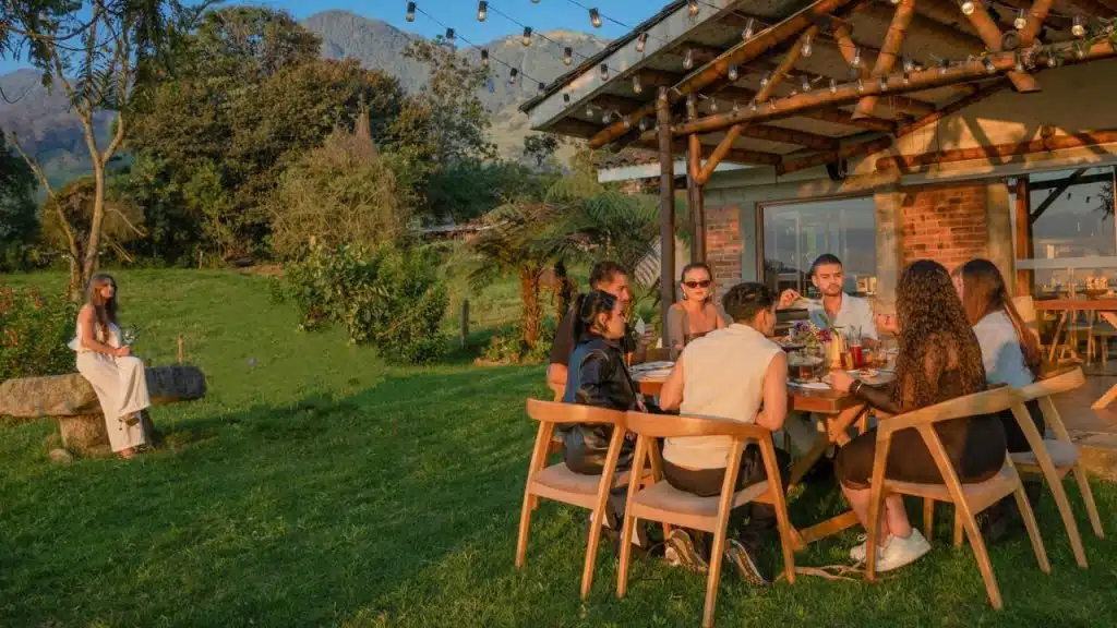 A group eats at a table while a woman sits alone on a rock nearby.