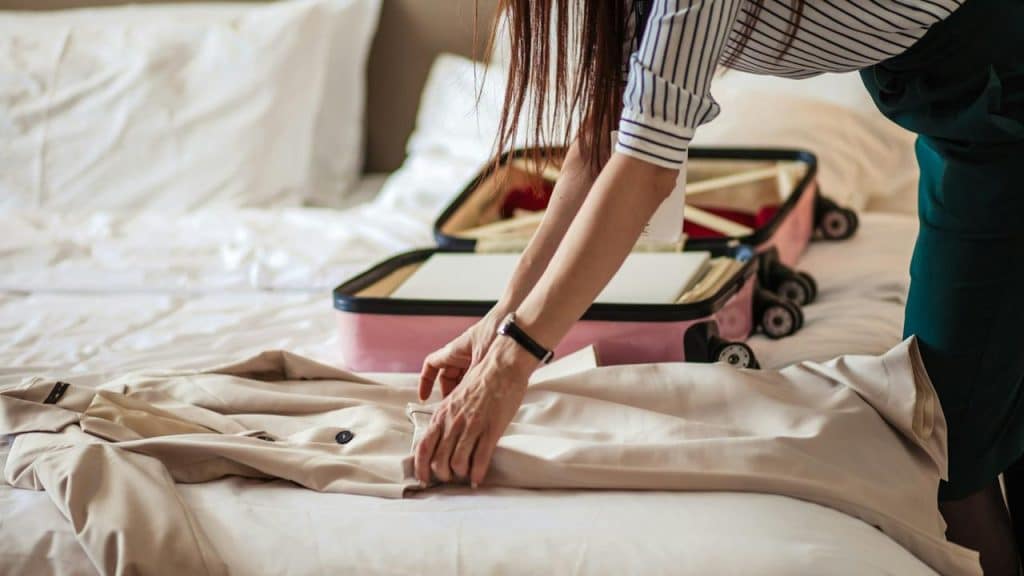 A woman folding clothes next to an open suitcase on a bed.