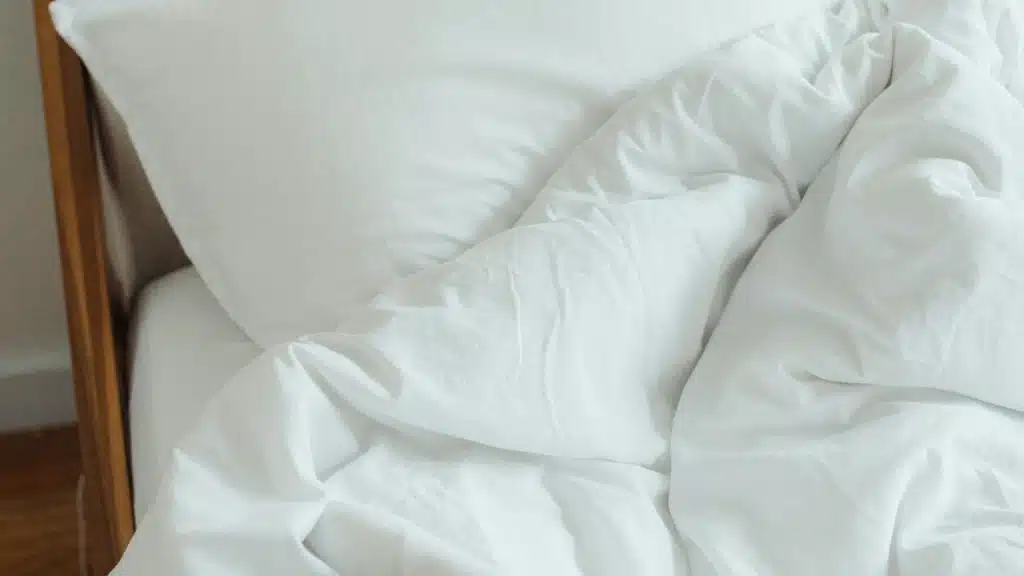A bed with white pillows and a crumpled white blanket.