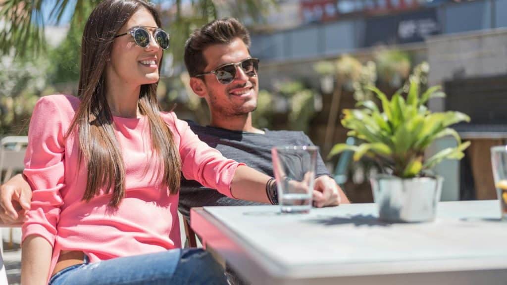A smiling couple wearing sunglasses, relaxing together at an outdoor café.