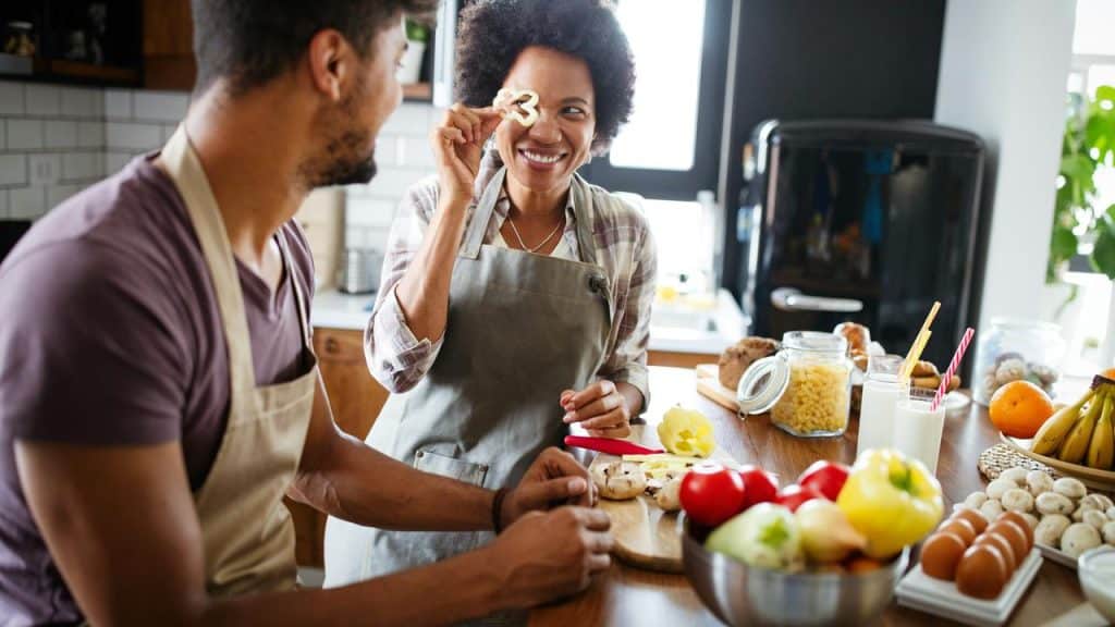 A couple cooking together in a kitchen and smiling playfully.