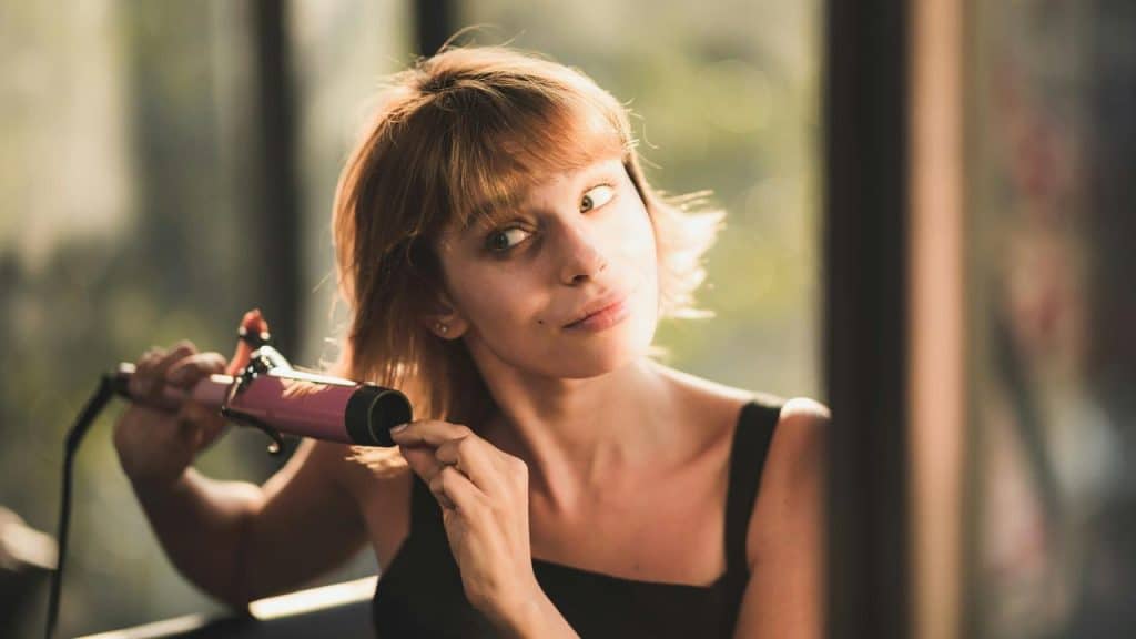 A woman curling her hair with a curling iron in warm indoor light.