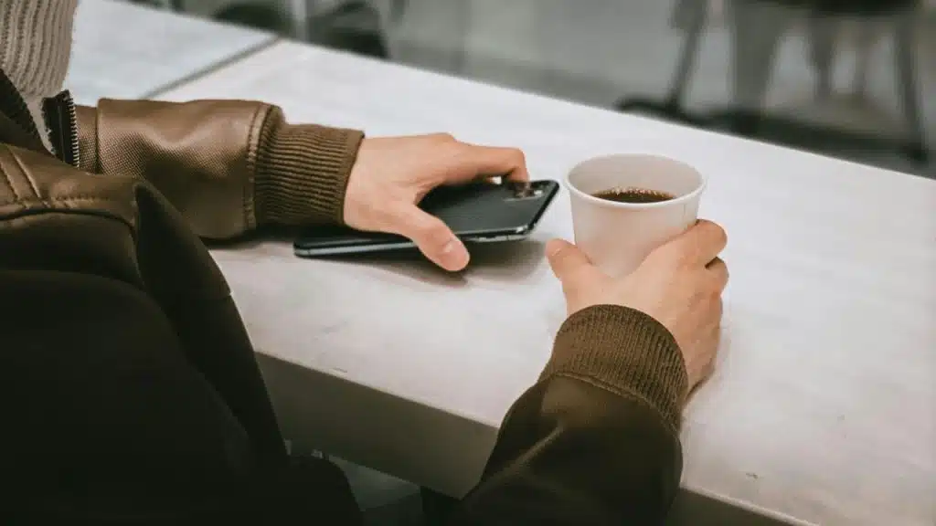 A person holding a cup of coffee in one hand and a smartphone in the other.