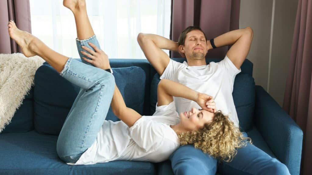 A woman lies on a man’s lap while they both relax on a blue couch.