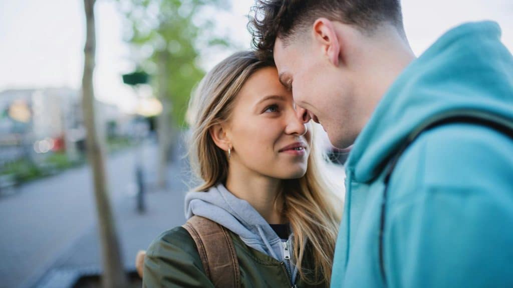 A young couple standing close together and smiling at each other outdoors.