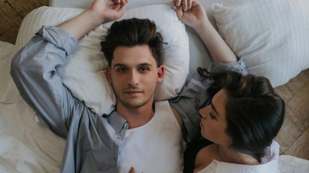 A man lies on a bed looking upward while a woman lies beside him.