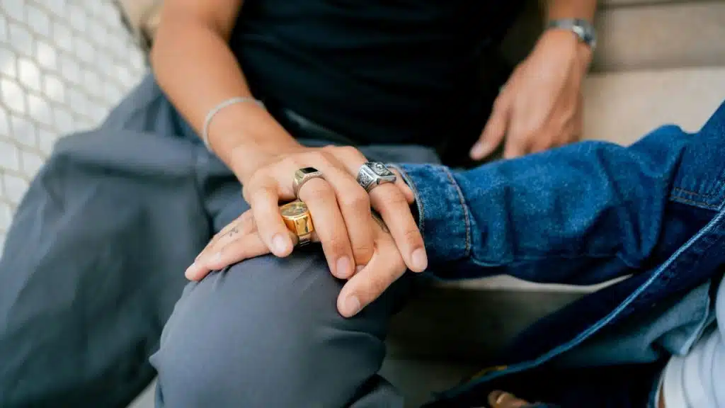 A close-up of a person’s hand resting on another person’s knee while they sit together.
