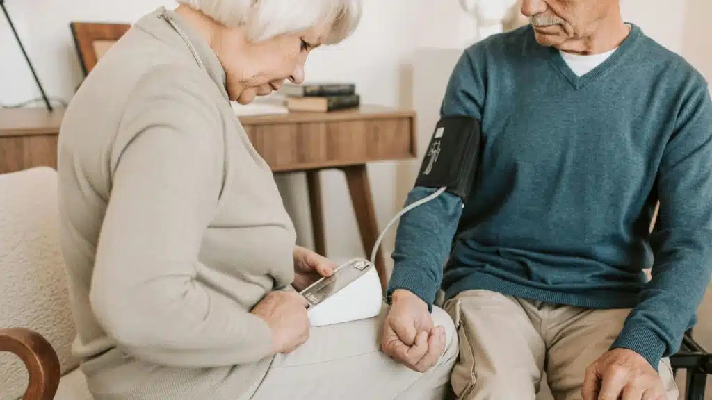 A woman uses a digital blood pressure monitor on the arm of a seated man.