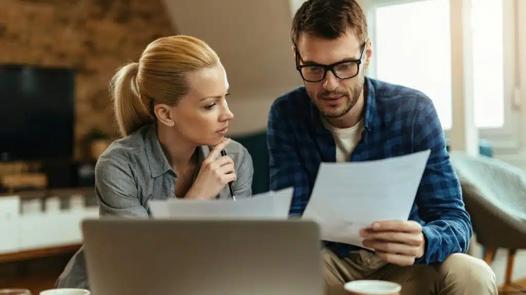 A woman with a ponytail and a man with glasses look at paper documents together.