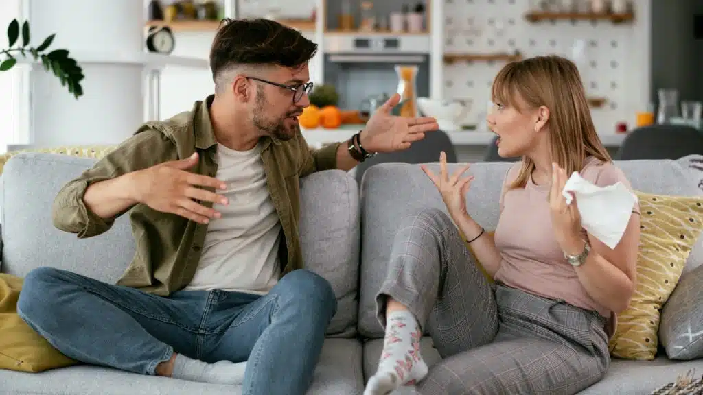A couple fighting while they are sitting together on a sofa at home.