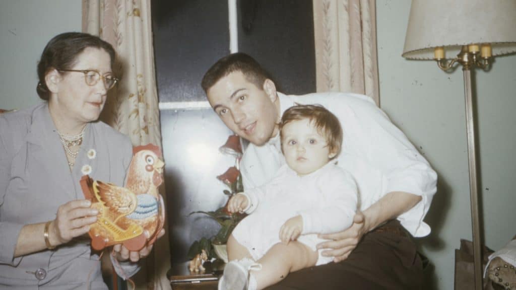 A man in a white shirt holding a baby while sitting near a woman inside a room.