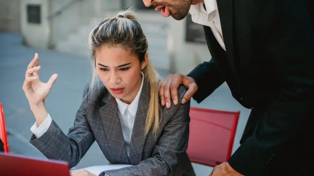 A woman in a suit looks at a laptop while a man stands behind her.