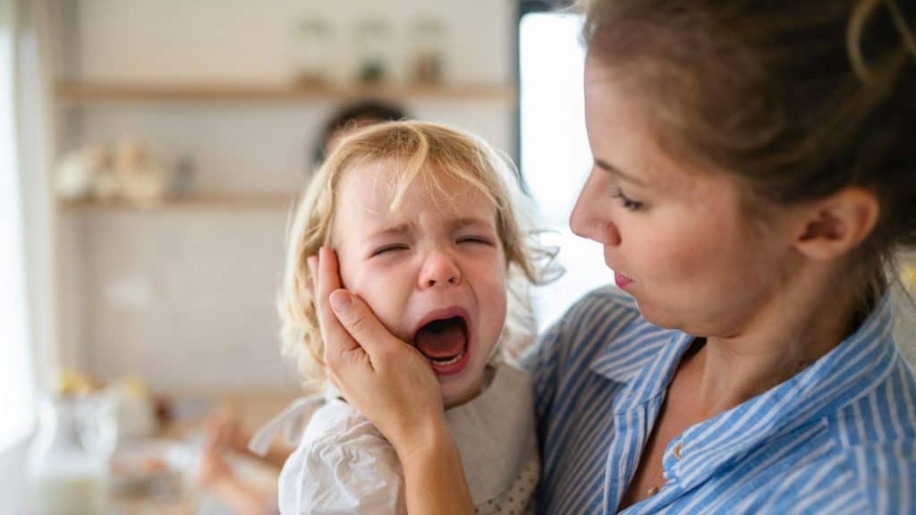 A woman holds a crying child's face in her hand while looking closely at them.