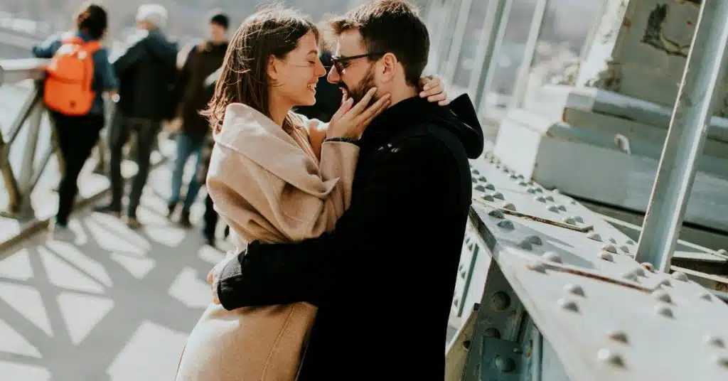 A couple embracing and smiling at each other on a city bridge.