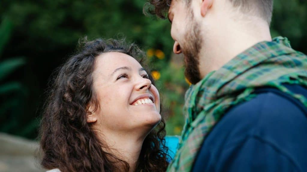 A woman smiling up at a man as they stand close together outdoors.