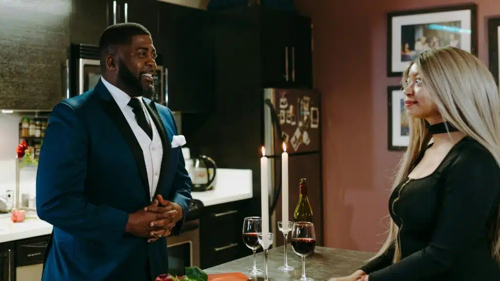 A man in a suit and a woman in black stand near wine and candles.