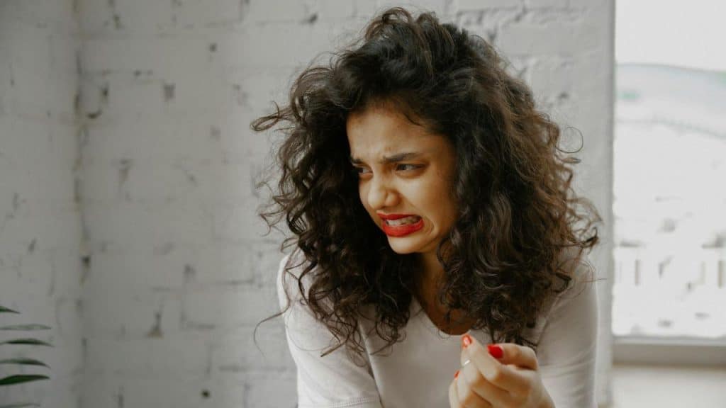 A woman with curly hair and red lipstick makes a grimacing facial expression.