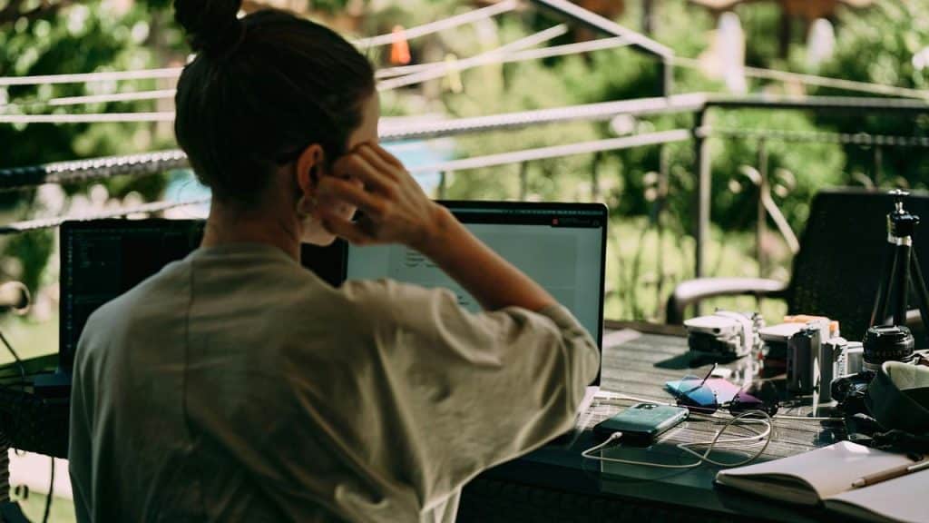 A person working on a laptop at an outdoor desk surrounded by greenery.