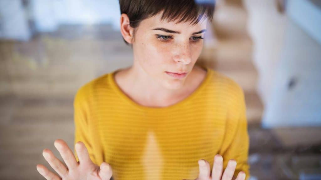 A woman with short hair looking thoughtfully through a glass surface.