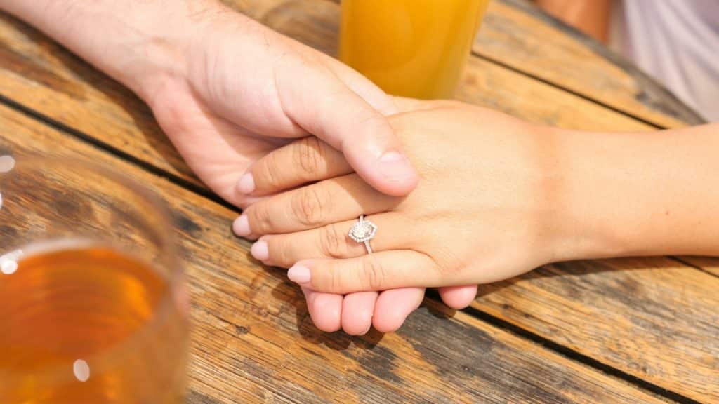 A close-up shot shows two people holding hands over a wooden table with drinks.
