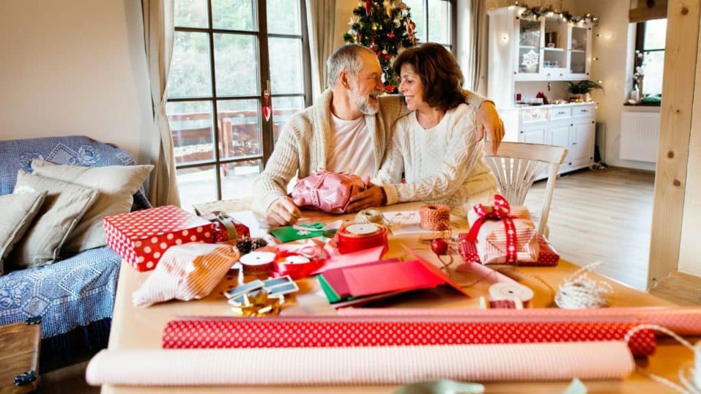 An older couple sits at a table covered in wrapping paper and holiday gifts.