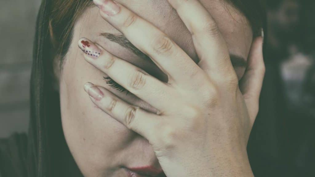A closeup of a woman covering her face with her hand.