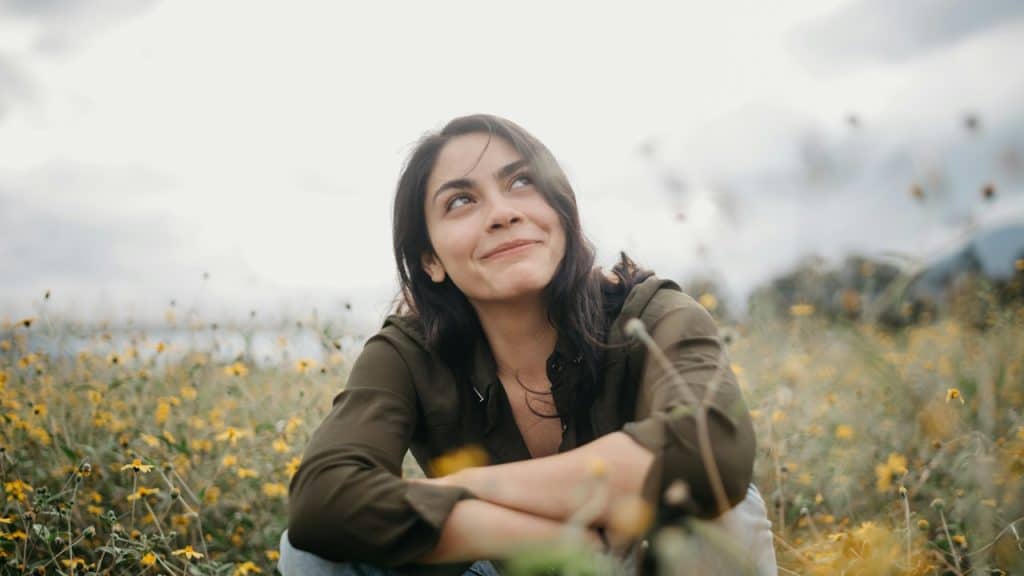A woman smiling and looking upwards while sitting in a field of wild flowers.