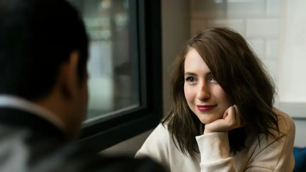 A woman smiling and staring at a man while holding her chin with her hand.