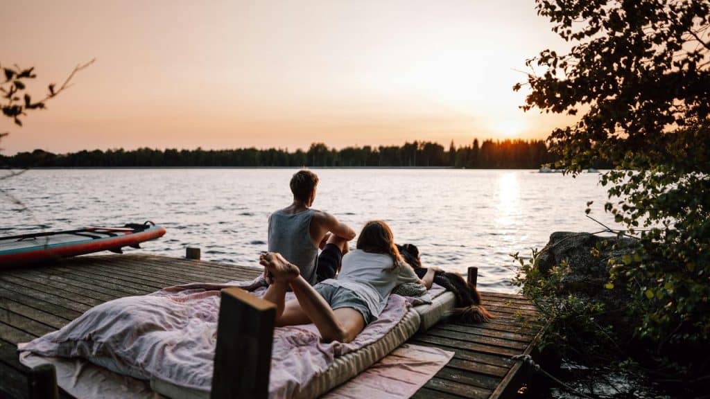 A couple relaxes on a dock mattress by the lake during sunset.