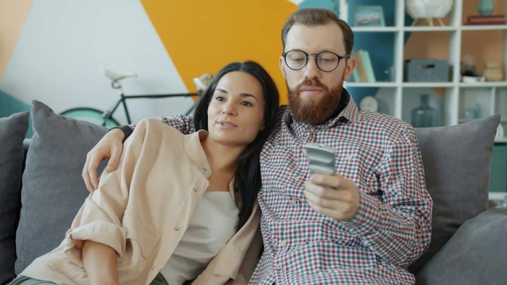 Couple sitting on couch, man holding TV remote.