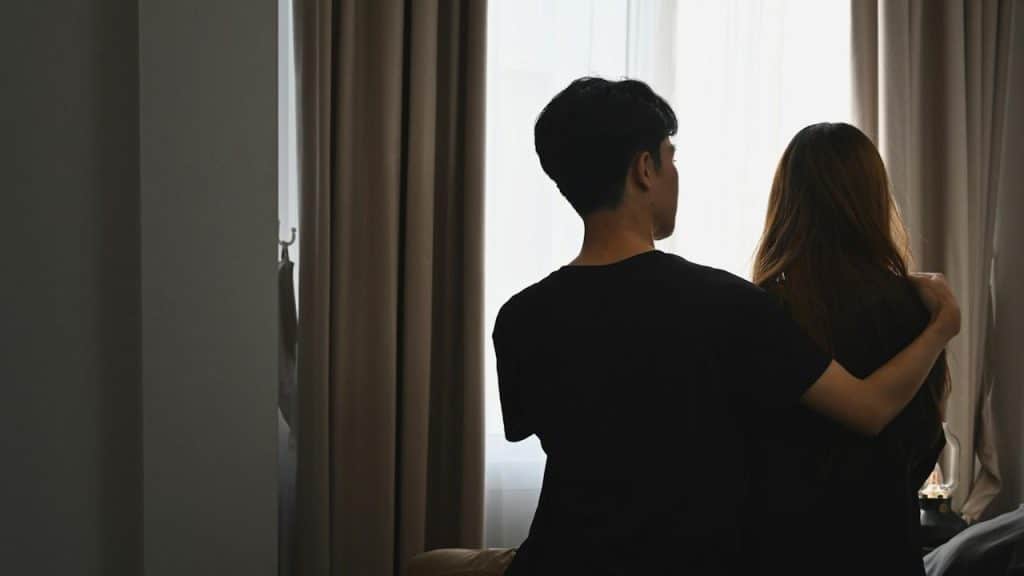 A young man is embracing his girlfriend and sitting in the bedroom.