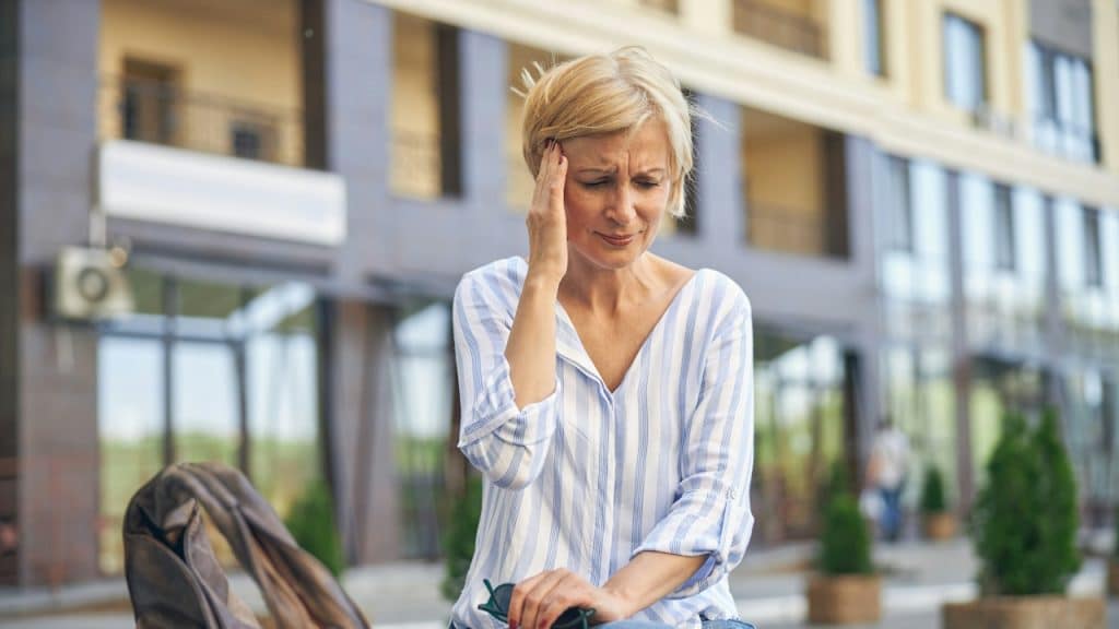 A depressed, cheerless, mature, short-haired, elegant Caucasian female with her hand on her temple, looking down.