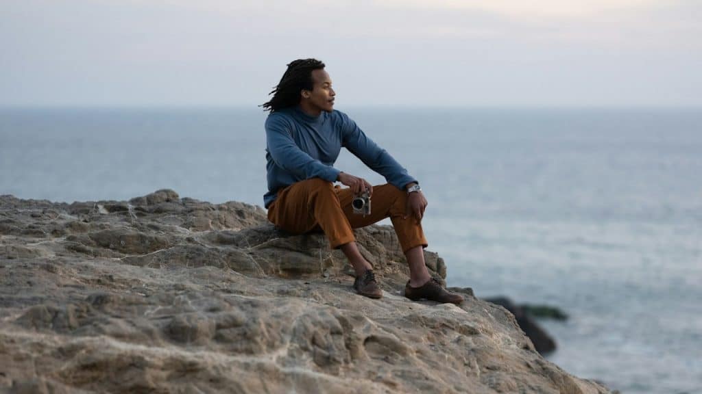 A man sitting on a big rock near a body of water.