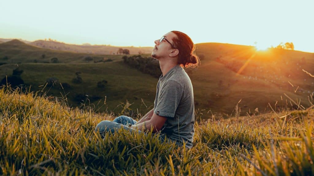 A man in a white shirt sitting on a green grass field during sunset.