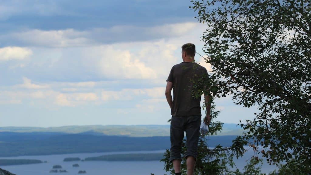 A man in a brown t-shirt standing on a rock near a green tree during daytime.