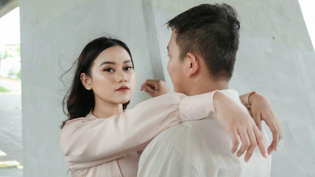A man looking at a woman and the  woman is looking in the camera while they are standing close to each other.