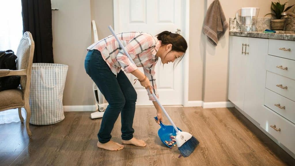 A woman sweeping the floor with a broom and dustpan in a kitchen.