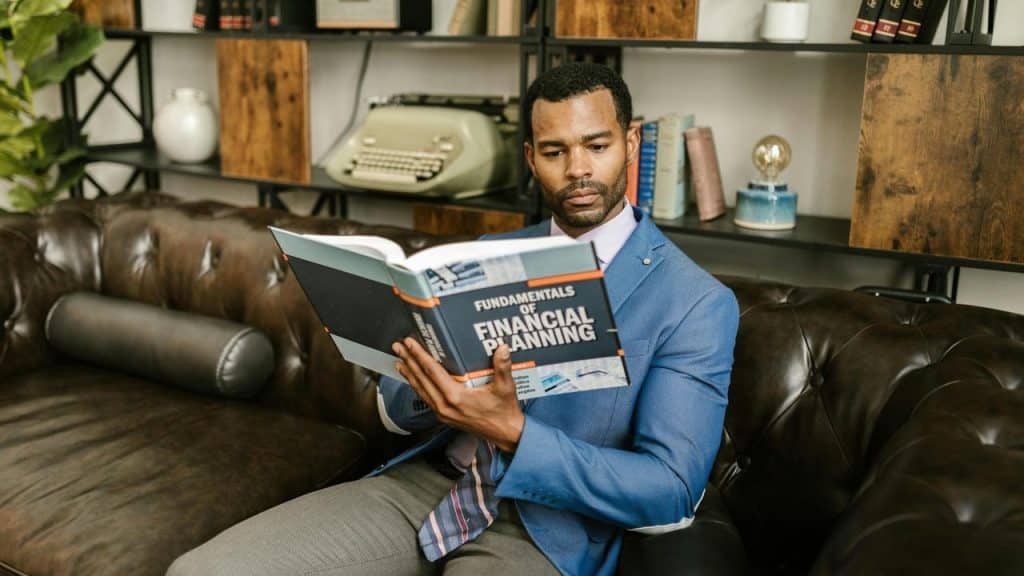A man in a suit reading a financial planning book on a leather couch.