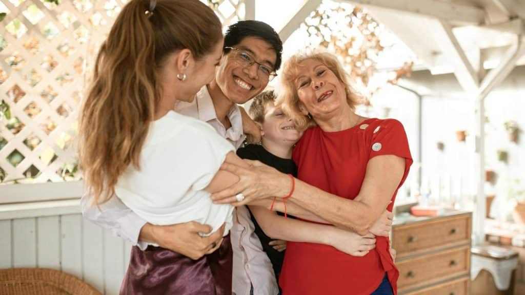 A smiling family hugging together on a sunny porch.